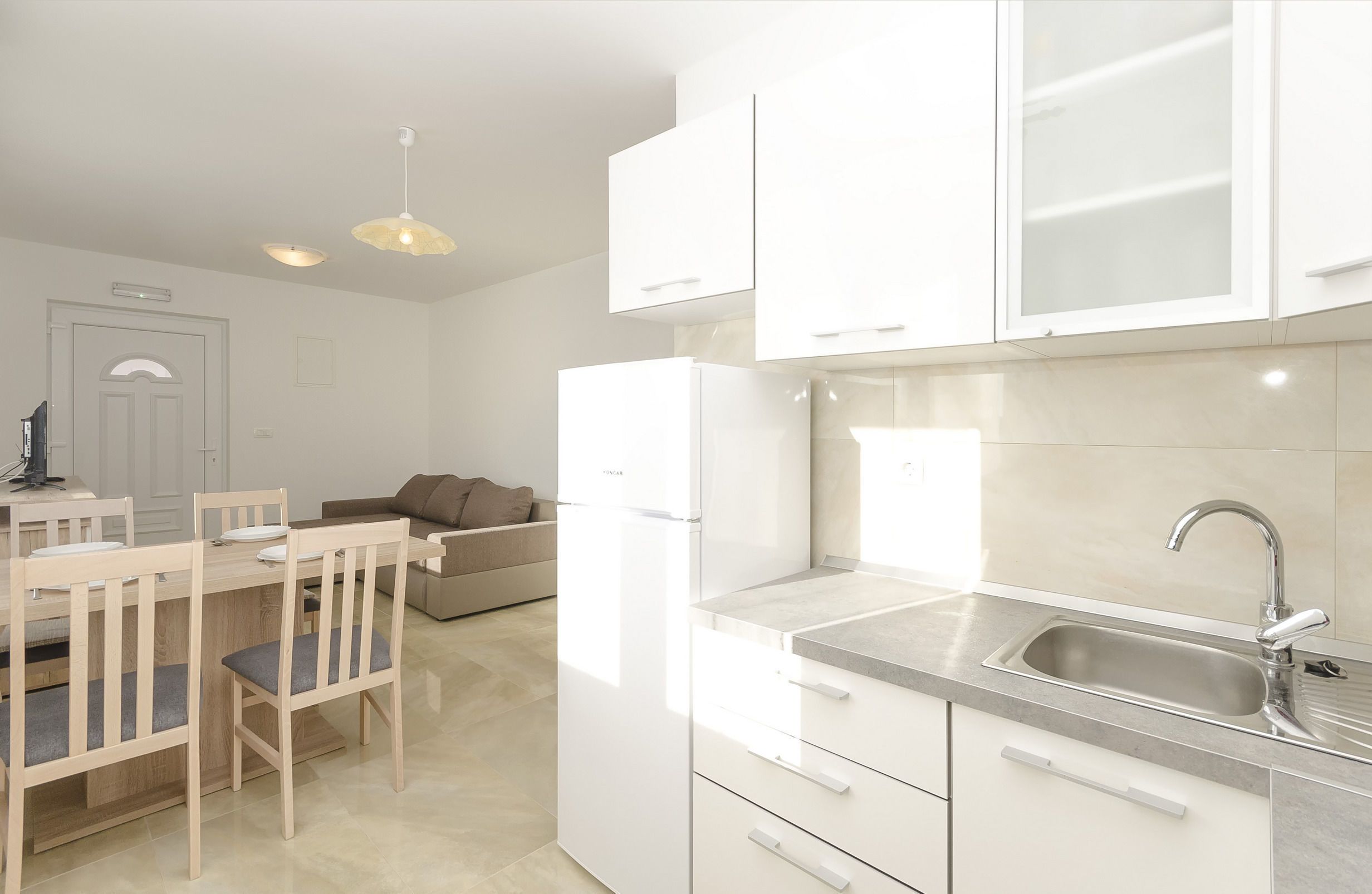 A modern kitchen with white cabinets, a stainless steel sink, and a dining area with wooden chairs and a table.