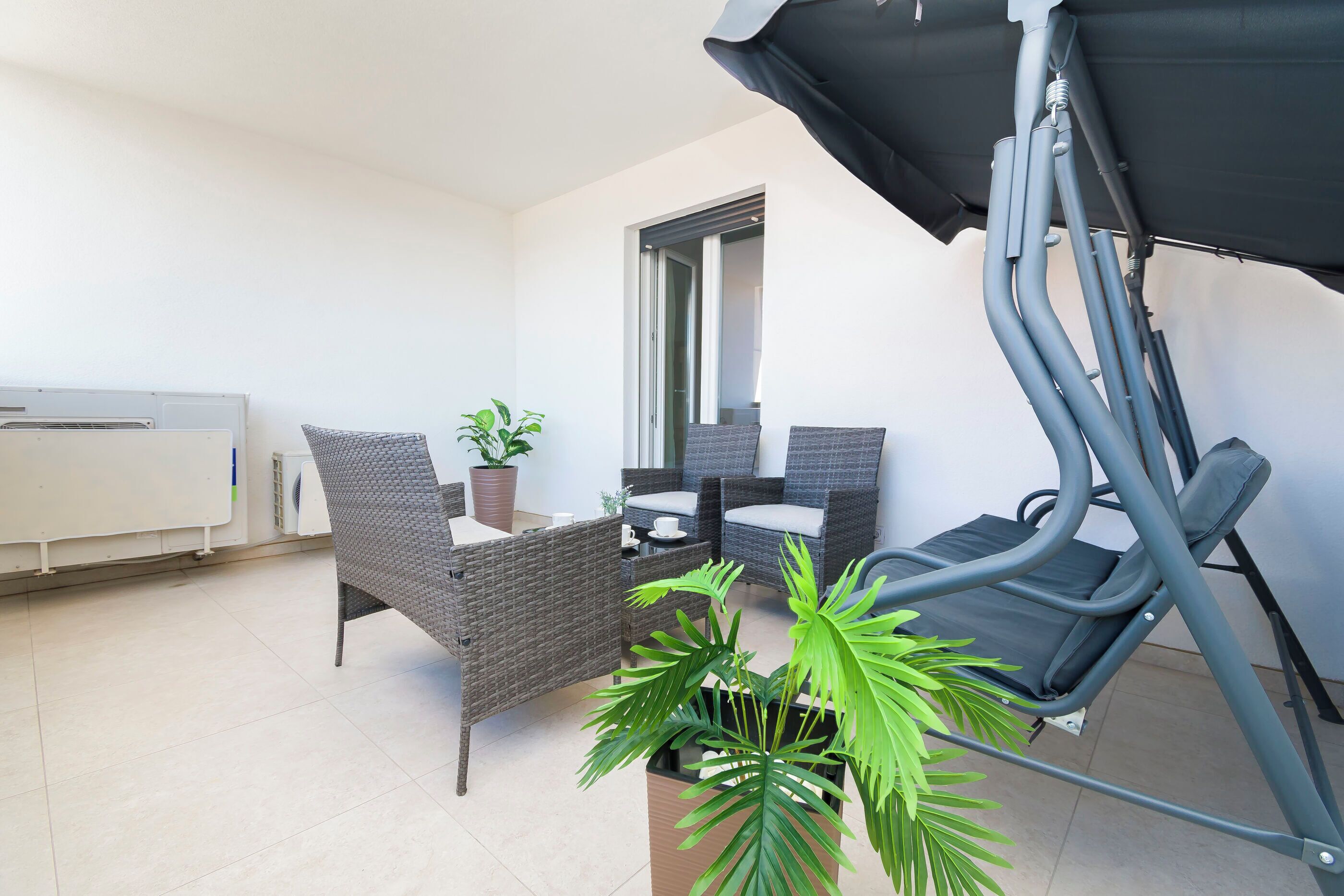 Een balkon met rieten meubilair, een plant in pot en een uitrolbaar zonnescherm.