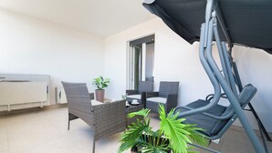 Ein Balkon mit Korbmöbeln, einer Topfpflanze und einem ausrollbaren Sonnensegel.