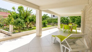 A covered outdoor area with a patio, green chairs, a white lounge chair, and a table. - Apartment Bakovic (Rogoznica)