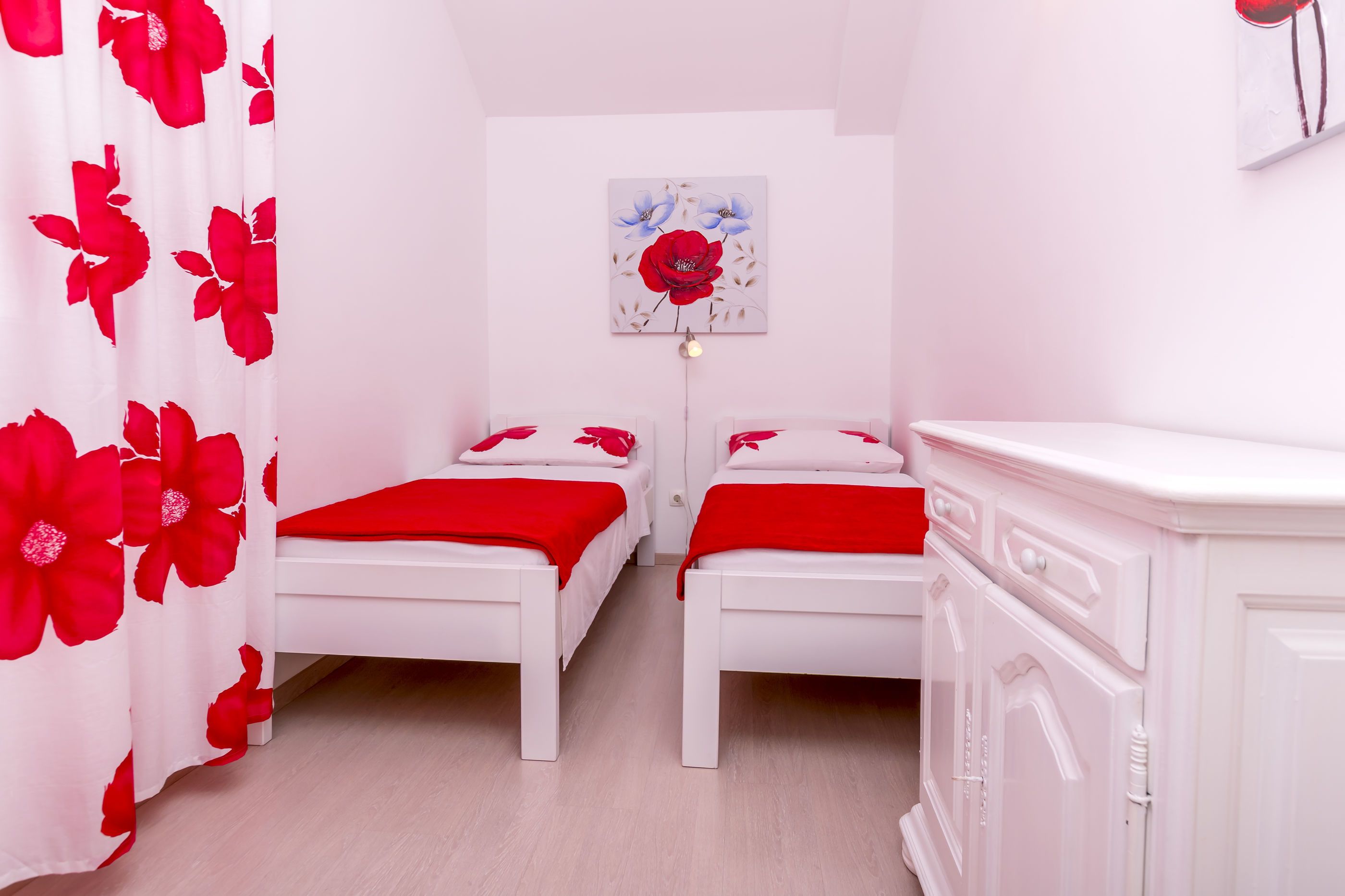 A bedroom with two beds, a white wardrobe, and a floral painting on the wall.