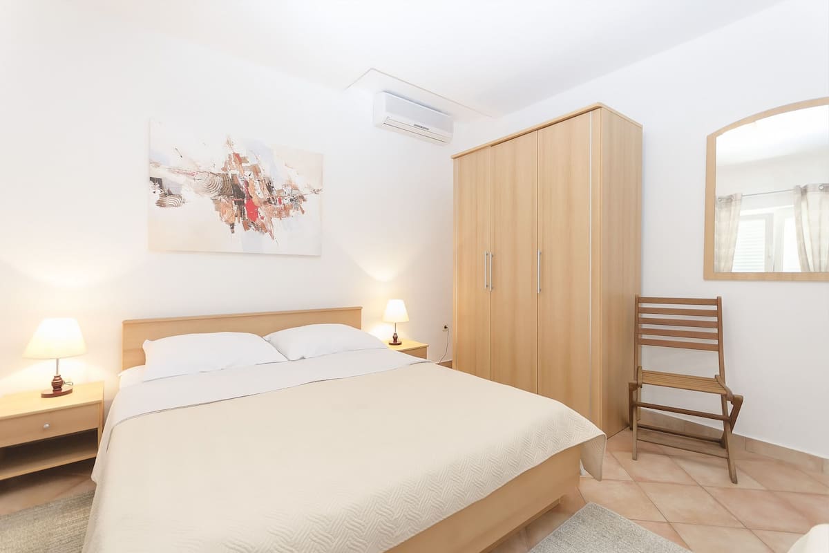 Une chambre à coucher comprenant un lit, une armoire en bois, des lampes de chevet, une chaise et un miroir fixé au mur.