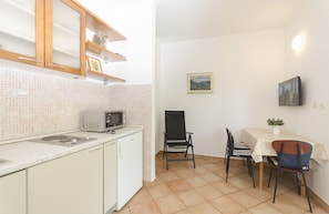 A compact kitchen with a microwave, a small sink, and a cabinet. There is a dining area with a table, chairs, and a potted plant. - Apartments Karolina (Vodice)