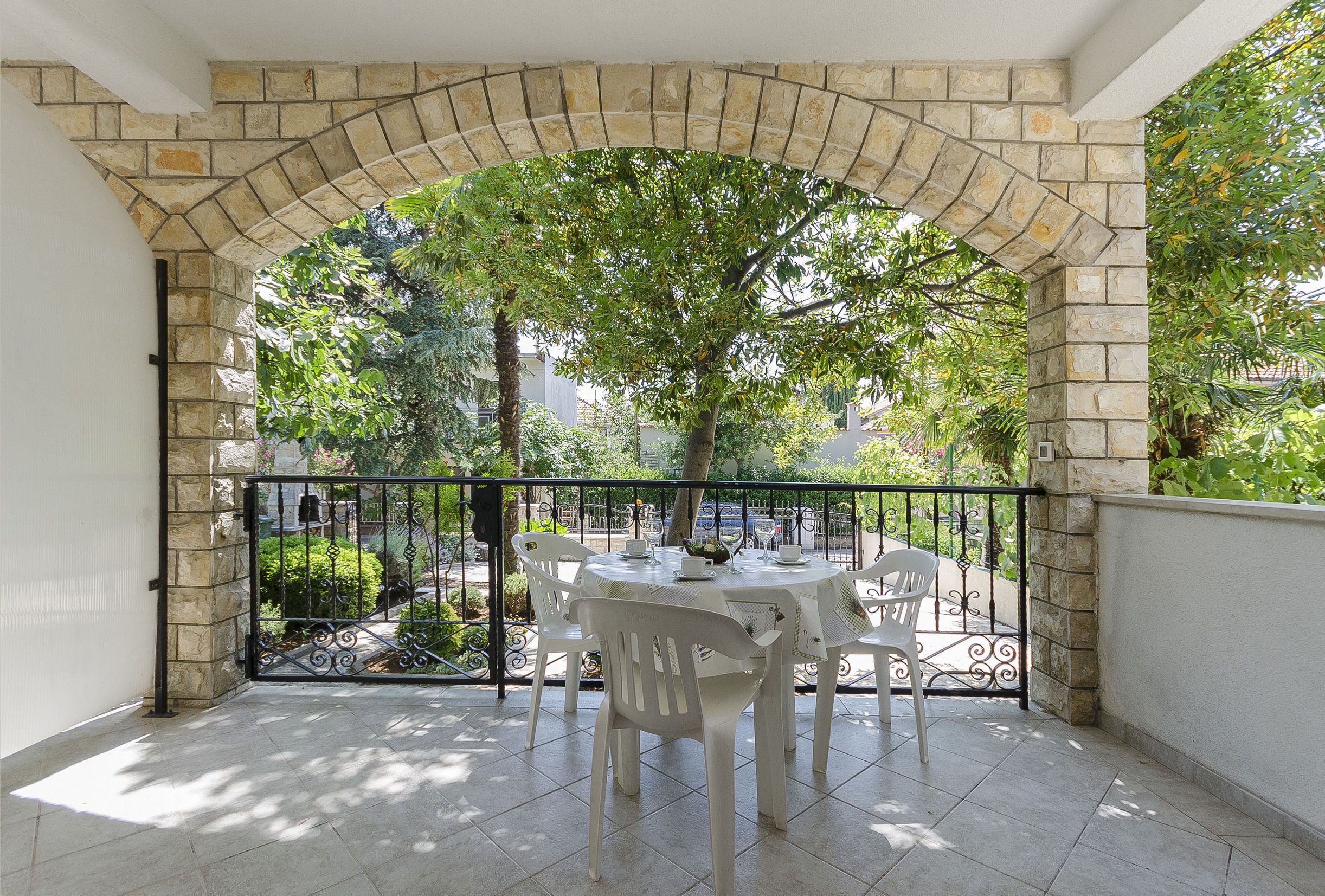 A patio with a stone archway, a table with chairs, and a view of greenery and buildings.