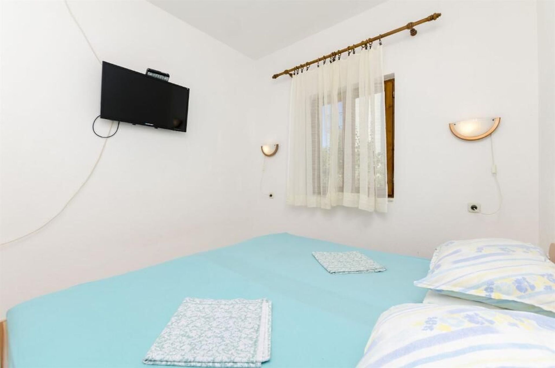 Een slaapkamer met een bed, een aan de muur bevestigde televisie en een raam met gordijnen.