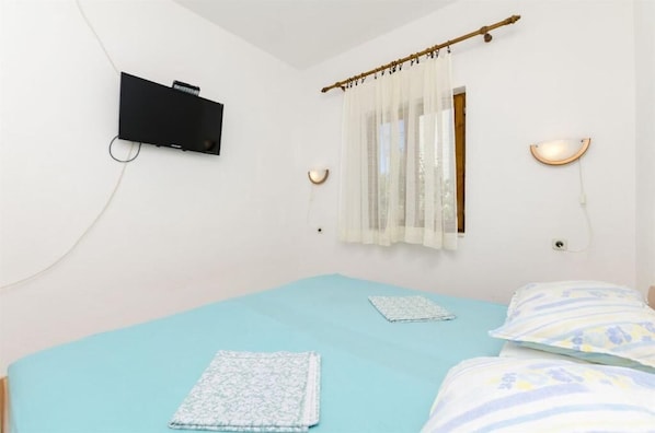 Una camera da letto con un letto singolo, una TV a muro e una finestra con tende leggere.