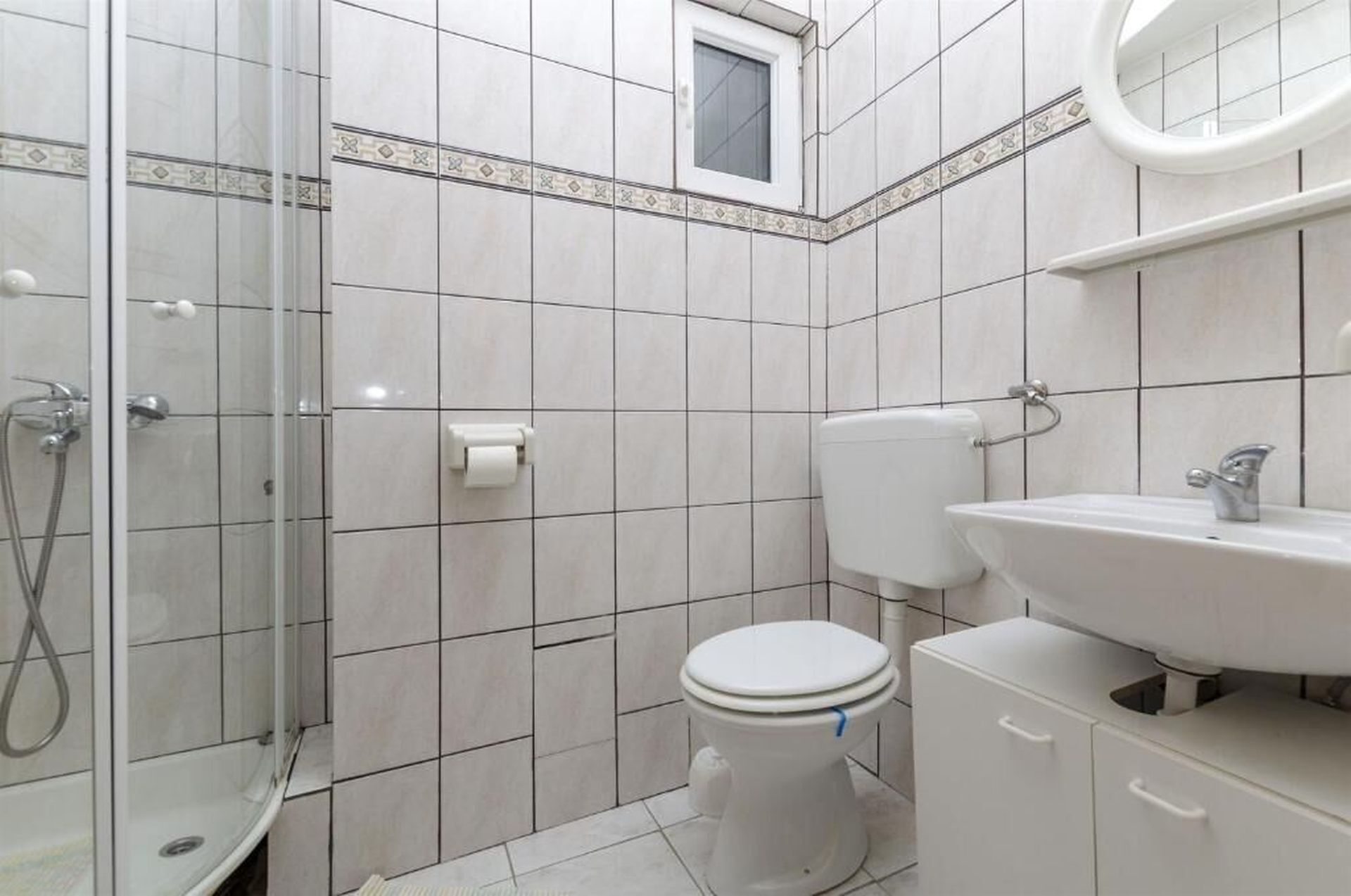 Une salle de bain avec une douche, des toilettes, un lavabo et une petite fenêtre.