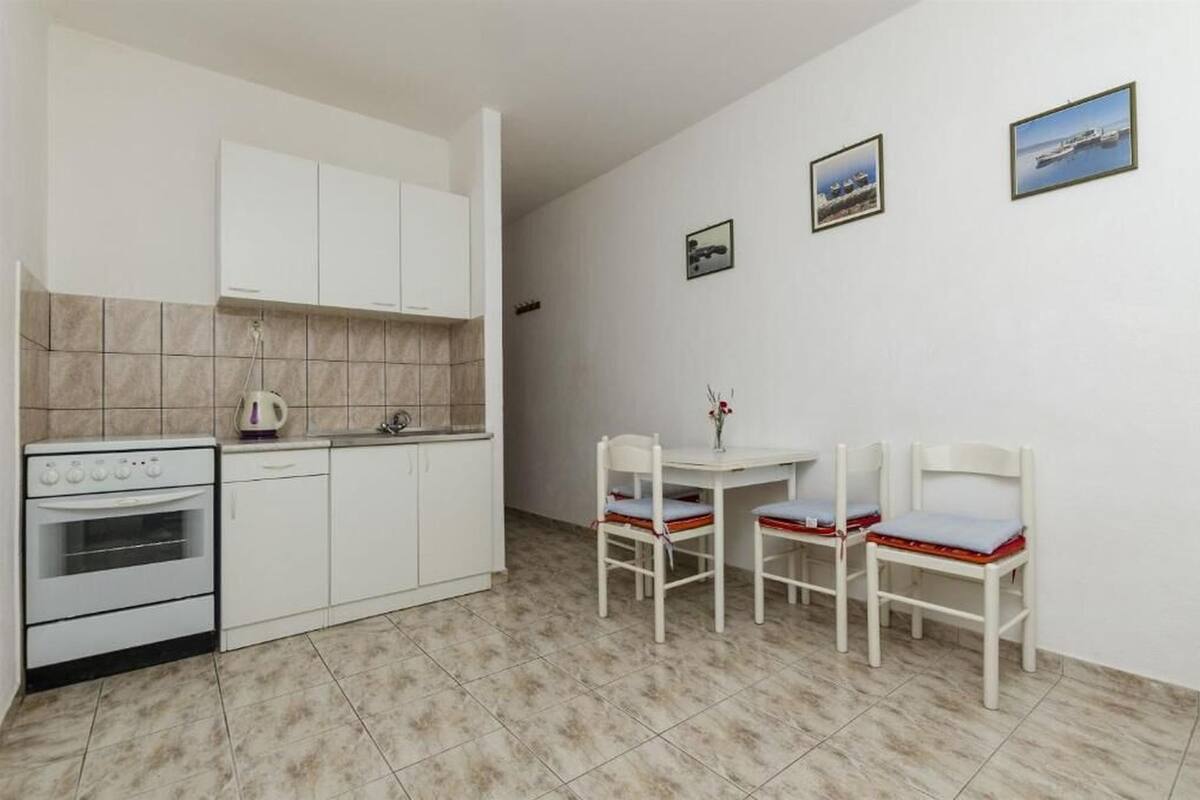 Une cuisine compacte avec des meubles blancs, une cuisinière et un plan de travail carrelé. On y trouve une petite table à manger avec quatre chaises.