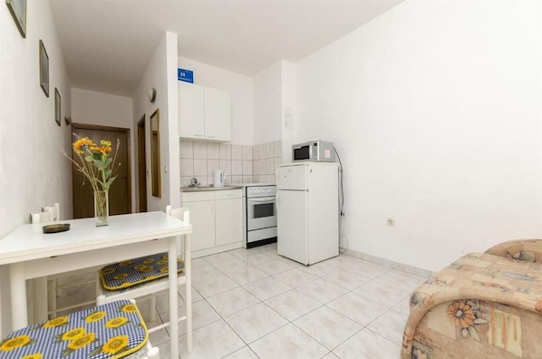 A compact kitchen with white cabinets, a microwave, and a stove. There is a small dining table with a vase of flowers. - Apartments Petra (Rogoznica)