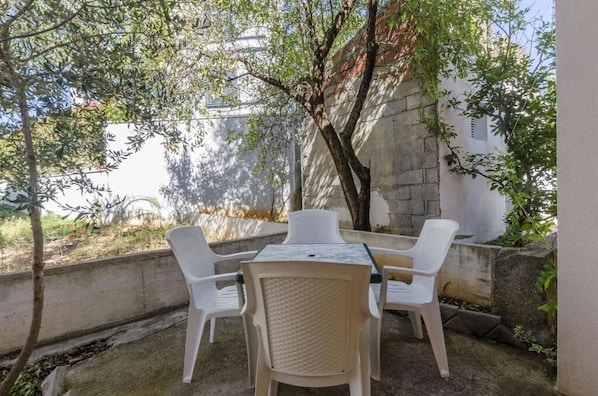 A patio with a table and four chairs, surrounded by trees and a stone wall. - Apartments Petra (Rogoznica)