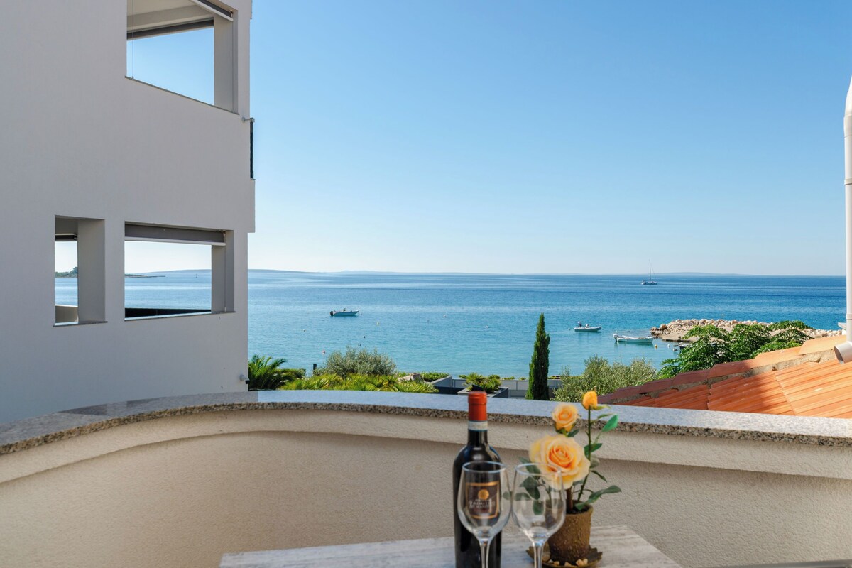 A balcony with a clear view of the sea, a bottle of wine, and a glass.