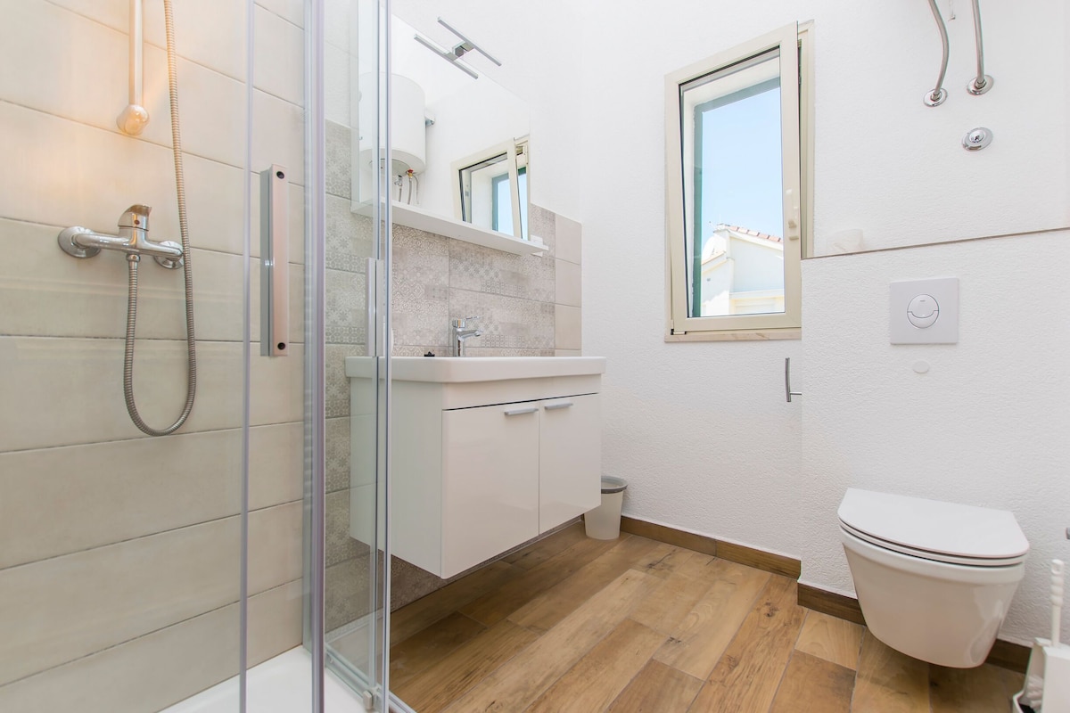 A modern bathroom with a glass shower enclosure, a white sink, and a toilet.