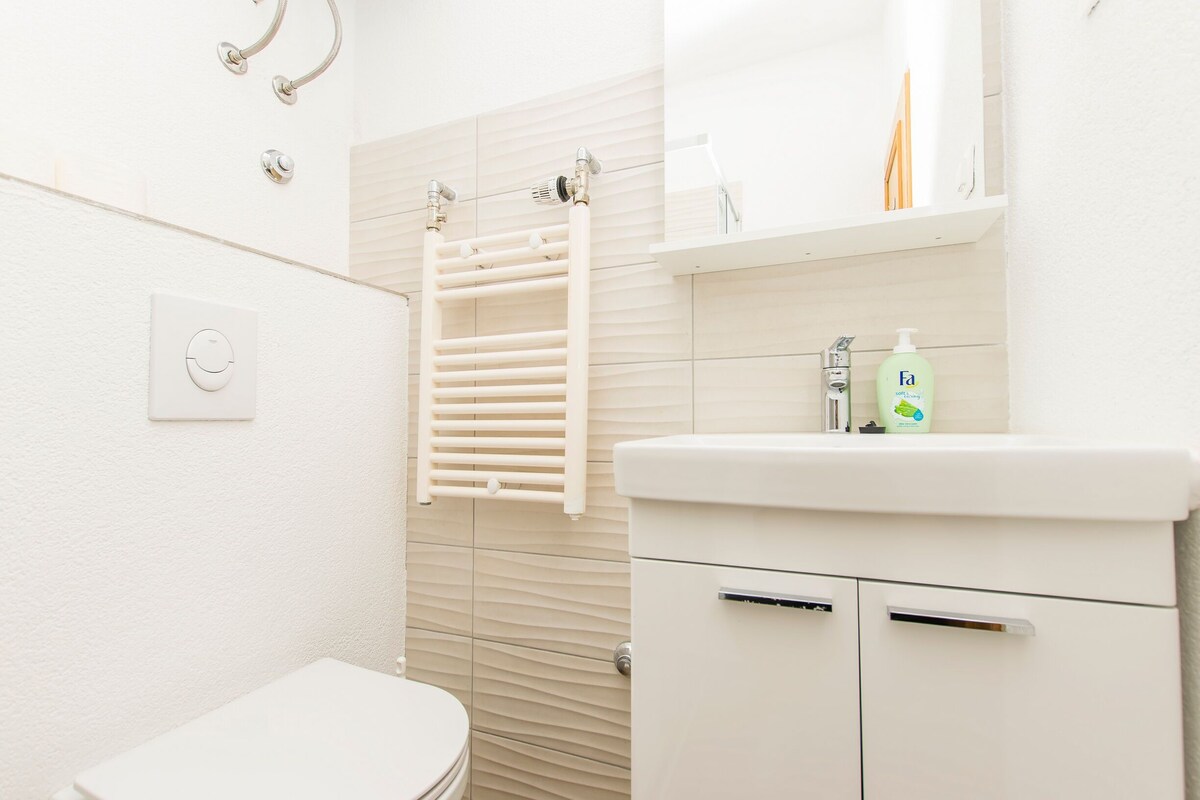 A modern bathroom with a toilet, a towel rack, a sink with toiletries, and a mirror.