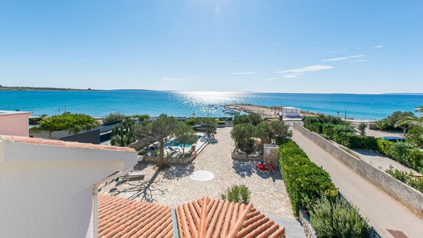 Blick auf die Küste mit blauem Himmel, einem Schwimmbad und einer Straße, die zum Strand führt.