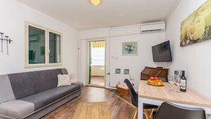 Ein modernes Wohnzimmer mit grauem Sofa, Holzboden, einem Esstisch mit Stühlen, einem Fernseher und einem Bild an der Wand.