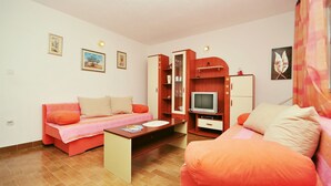 Ein gemütlicher Raum mit einer Sitzecke, einem kleinen Tisch, einem Fernseher und einem Schrank.