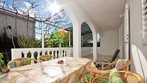 Eine Terrasse im Freien mit Tisch und Korbstühlen, umgeben von weißen Wänden und überdacht.