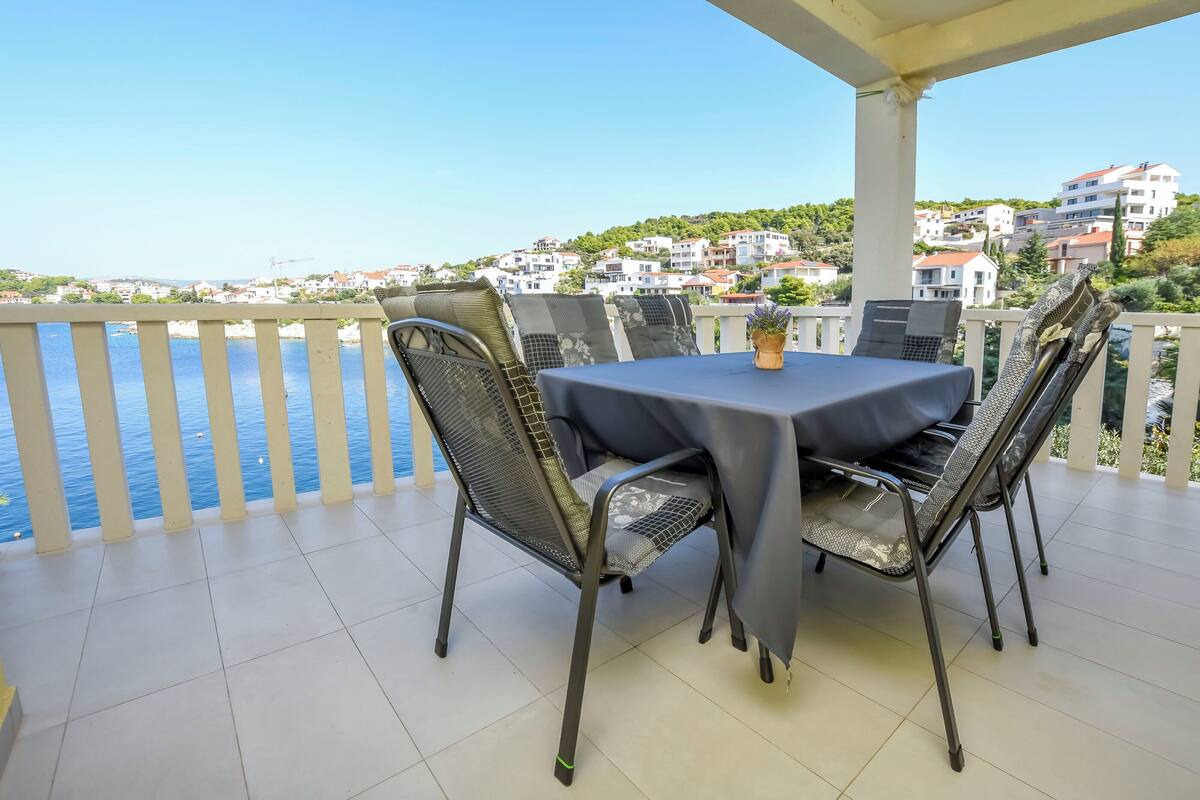 Una terrazza con tavolo e sedie, affacciata su una zona costiera con edifici sullo sfondo.