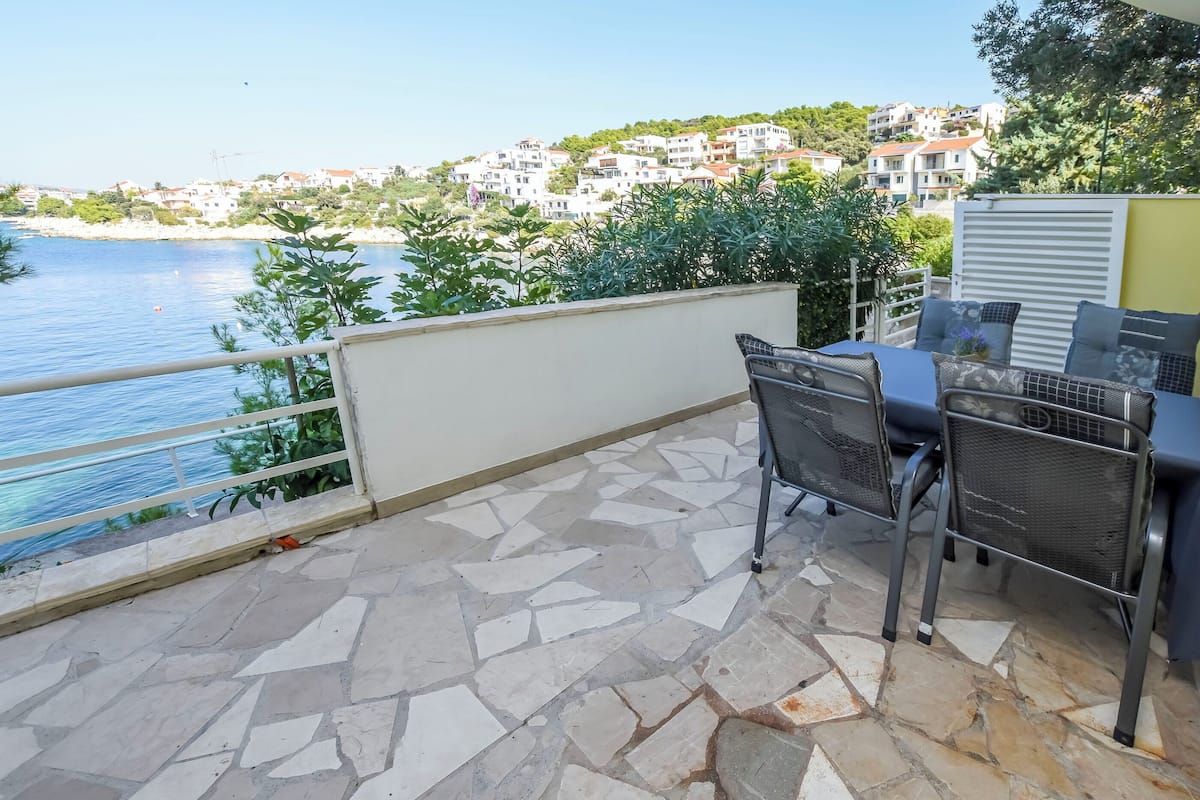 Una terrazza con pavimento in pietra, un tavolo con sedie e vista sul mare e sugli edifici sullo sfondo.