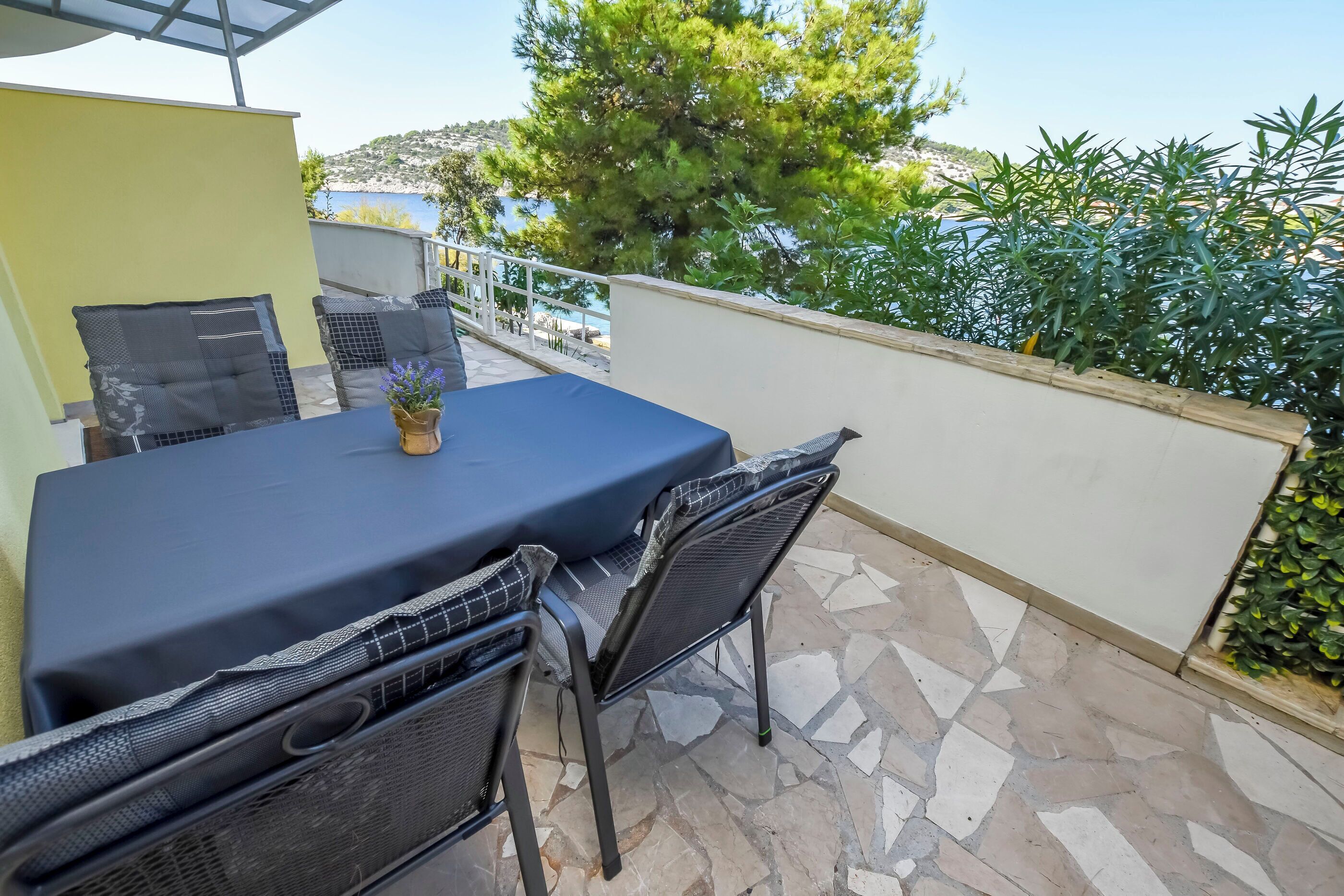 Une terrasse avec une table et des chaises, un pot de fleurs et une vue sur la mer et les collines.