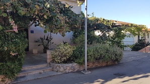 A building with a stone wall, steps leading to the entrance, and a pergola covered with vines. - Apartments and Room Caric (Jelsa)