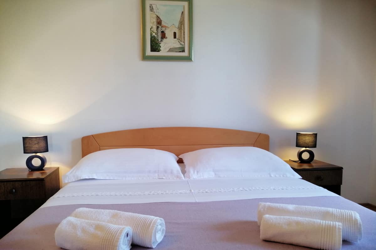 Un letto ben rifatto con lenzuola bianche, due asciugamani arrotolati sopra e due abat-jour su comodini.