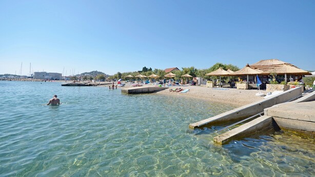 A beach with clear water, sun loungers, umbrellas, and a pier. - House Ivana Tribunj (Tribunj)