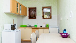 A compact kitchen with wooden cabinets, a microwave, a sink, and a dining area with chairs. - House Ivana Tribunj (Tribunj)