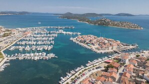An aerial view of a marina with numerous boats docked, a small island with buildings, and a clear blue sea. - House Ivana Tribunj (Tribunj)