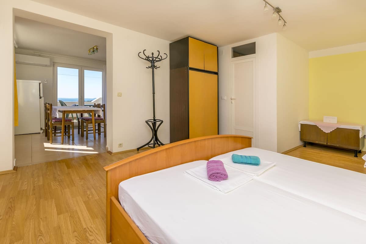 A hotel room with a bed, a dining area with a table and chairs, a coat stand, and a wardrobe.