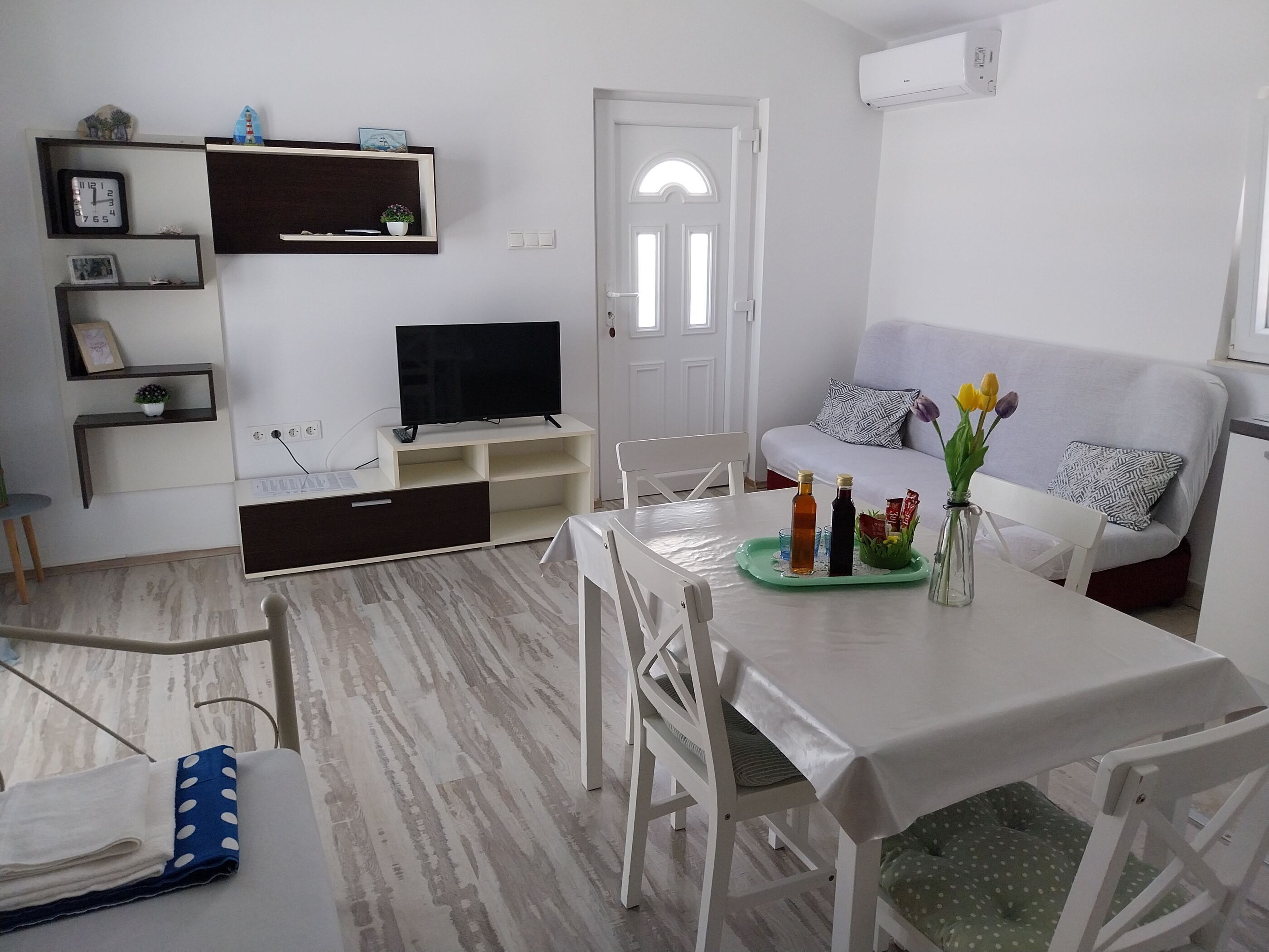 Un salon moderne avec un canapé blanc, une table à manger surmontée d’un plateau vert et un téléviseur posé sur un meuble.