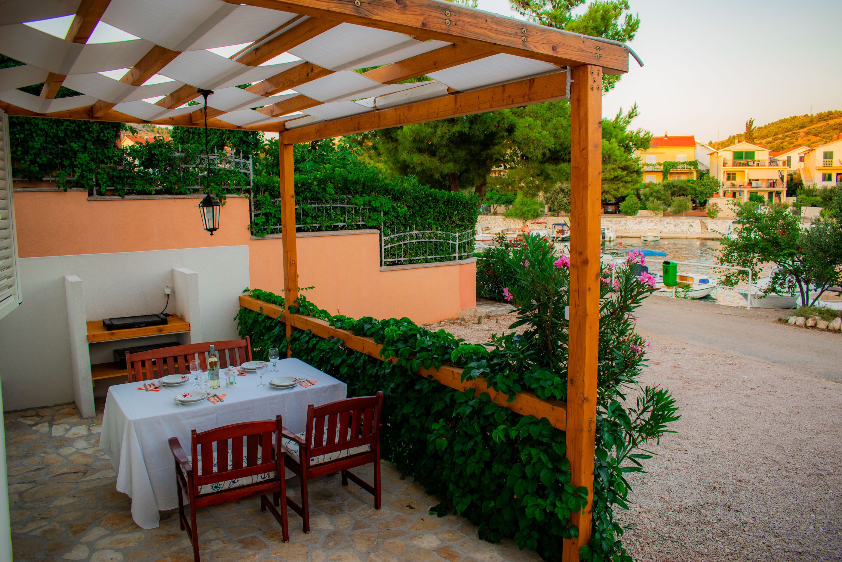 An outdoor patio with a table set for dining, surrounded by greenery and overlooking a body of water.