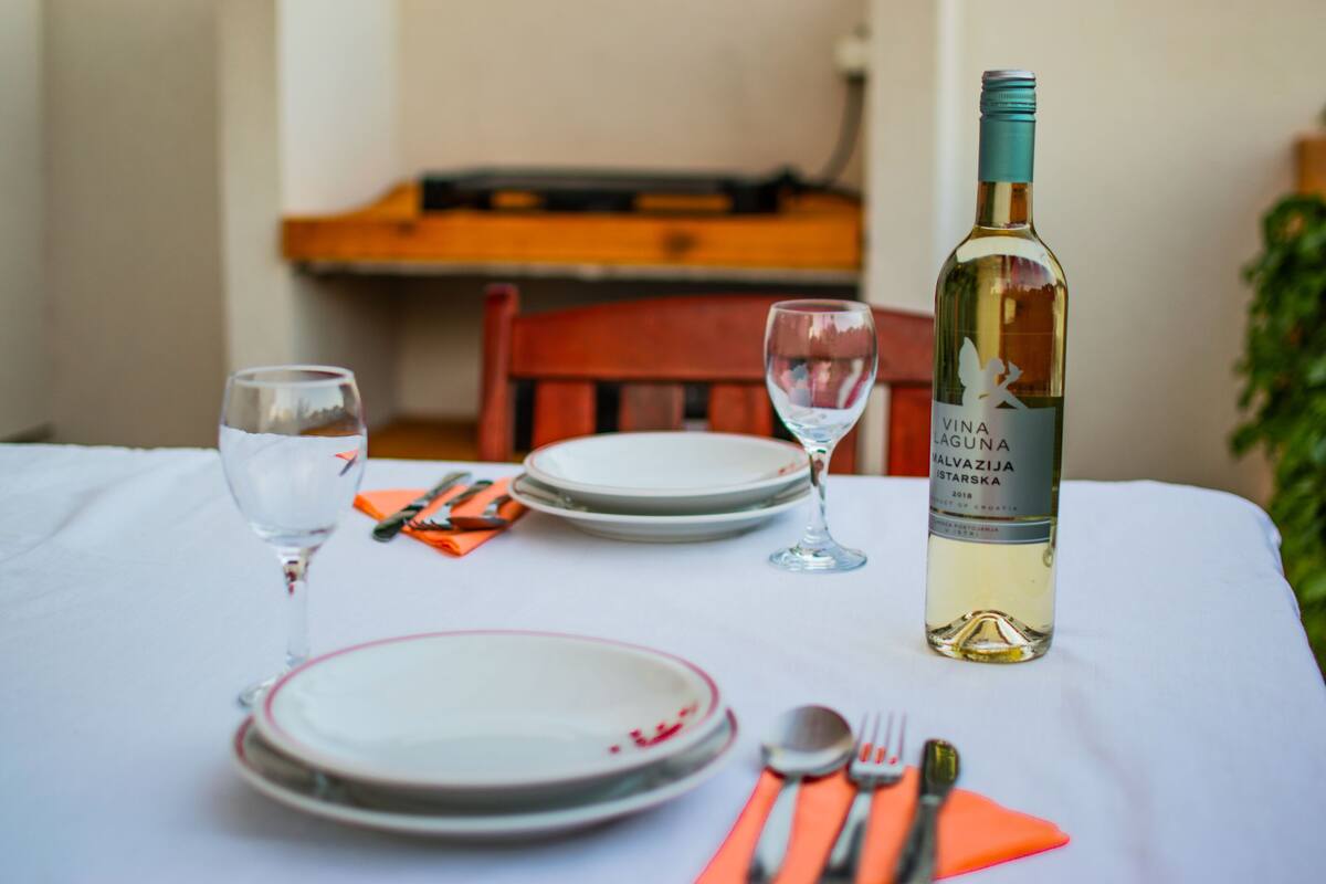 A dining table set with plates, cutlery, and a bottle of white wine.