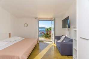 A hotel room with a bed, a sofa, a TV, and a balcony with a view of the sea.