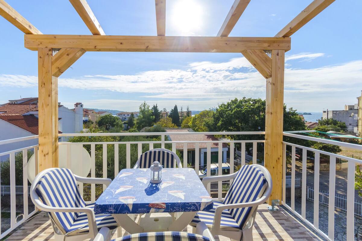 A wooden pergola with a table and chairs on a balcony overlooking a residential area.