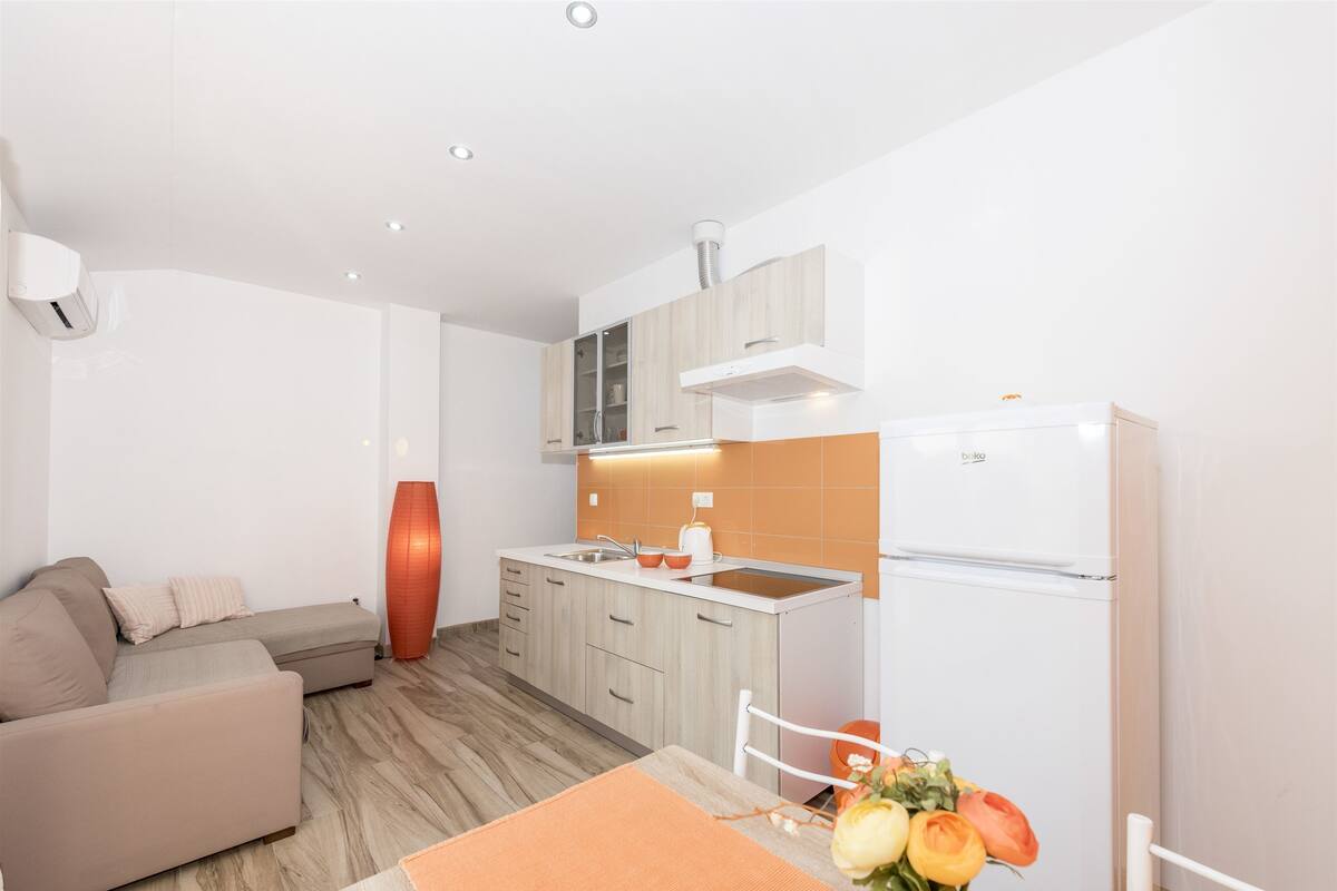 A modern kitchen with a built-in oven, a dining area with a table and chairs, and a sofa in the living area.