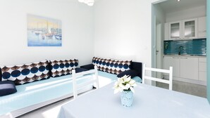 Una sala moderna con un sofá blanco, una mesa de comedor con un jarrón de flores y una zona de cocina con armarios blancos y un salpicadero azul.