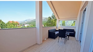 A balcony with a sofa and chairs, wooden flooring, and a view of mountains and houses. - Apartments Branka (Starigrad - Paklenica)