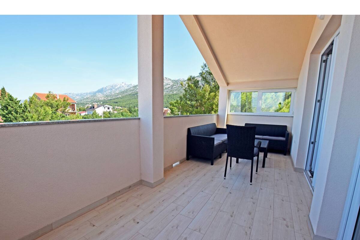 Un balcon avec un canapé et une table, un plancher en bois et une vue sur les montagnes et les maisons.