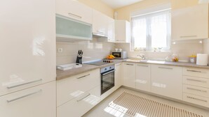 A modern kitchen with white cabinets, a built-in oven, a microwave, and a window providing natural light. - Apartments Luxury and Sea View (Brodarica)