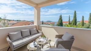 A balcony with a sofa, wicker chairs, a small table with cups and a plant, and a view of houses and trees. - Apartments Luxury and Sea View (Brodarica)