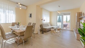 A modern living room with a dining area, a sofa, and a TV stand. - Apartments Luxury and Sea View (Brodarica)