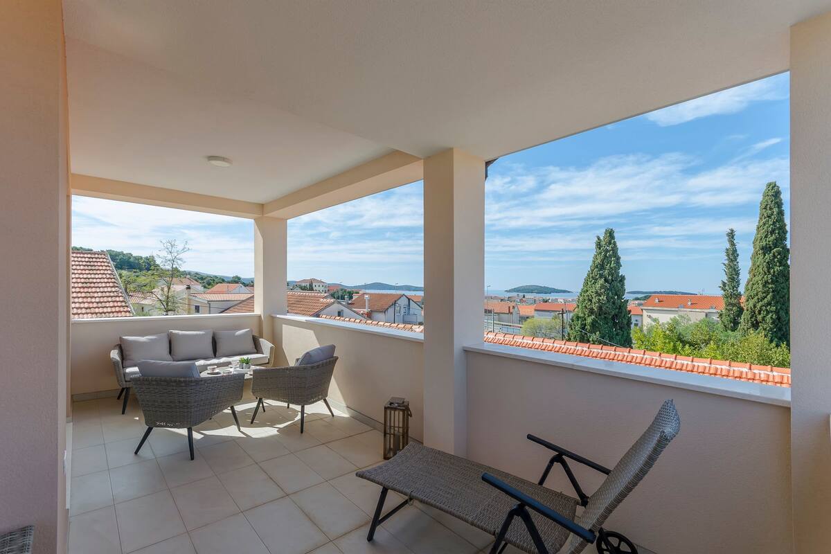 A balcony with wicker furniture, a view of the cityscape, and a clear sky.