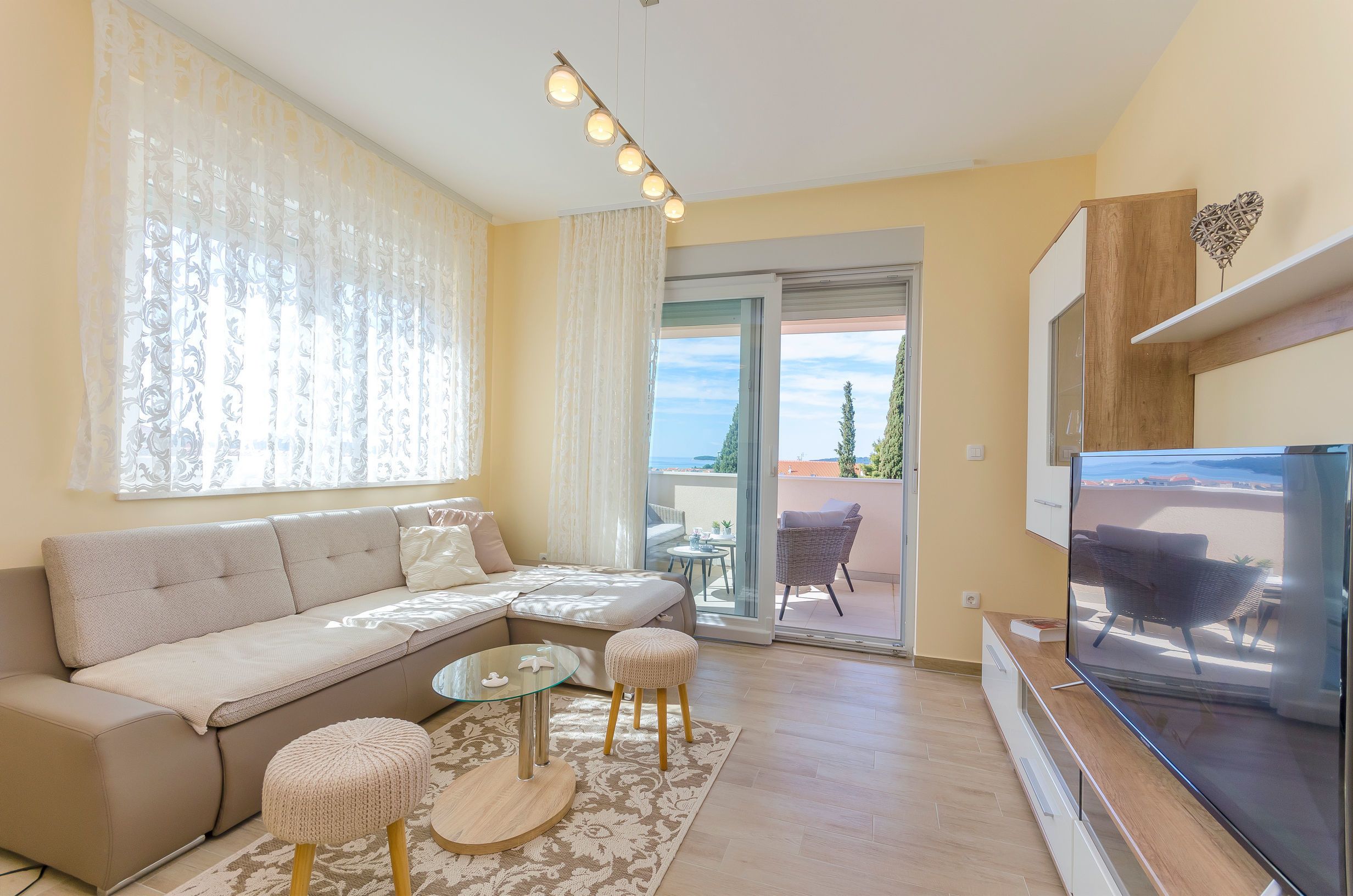 Un salon comprenant un canapé, un pouf, une table basse en verre et un téléviseur à écran plat.