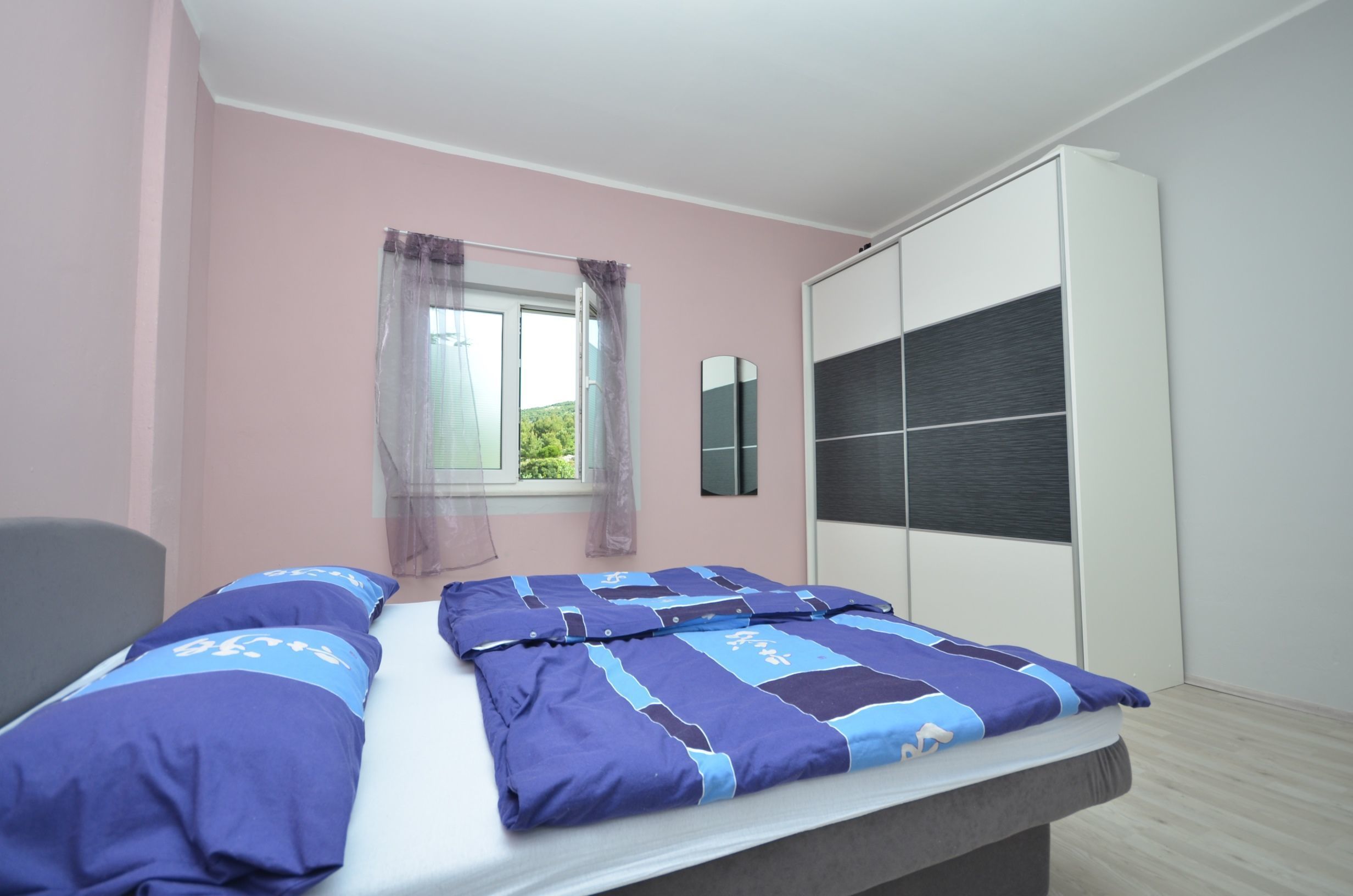 A bedroom with a bed, a wardrobe, and a window with curtains.