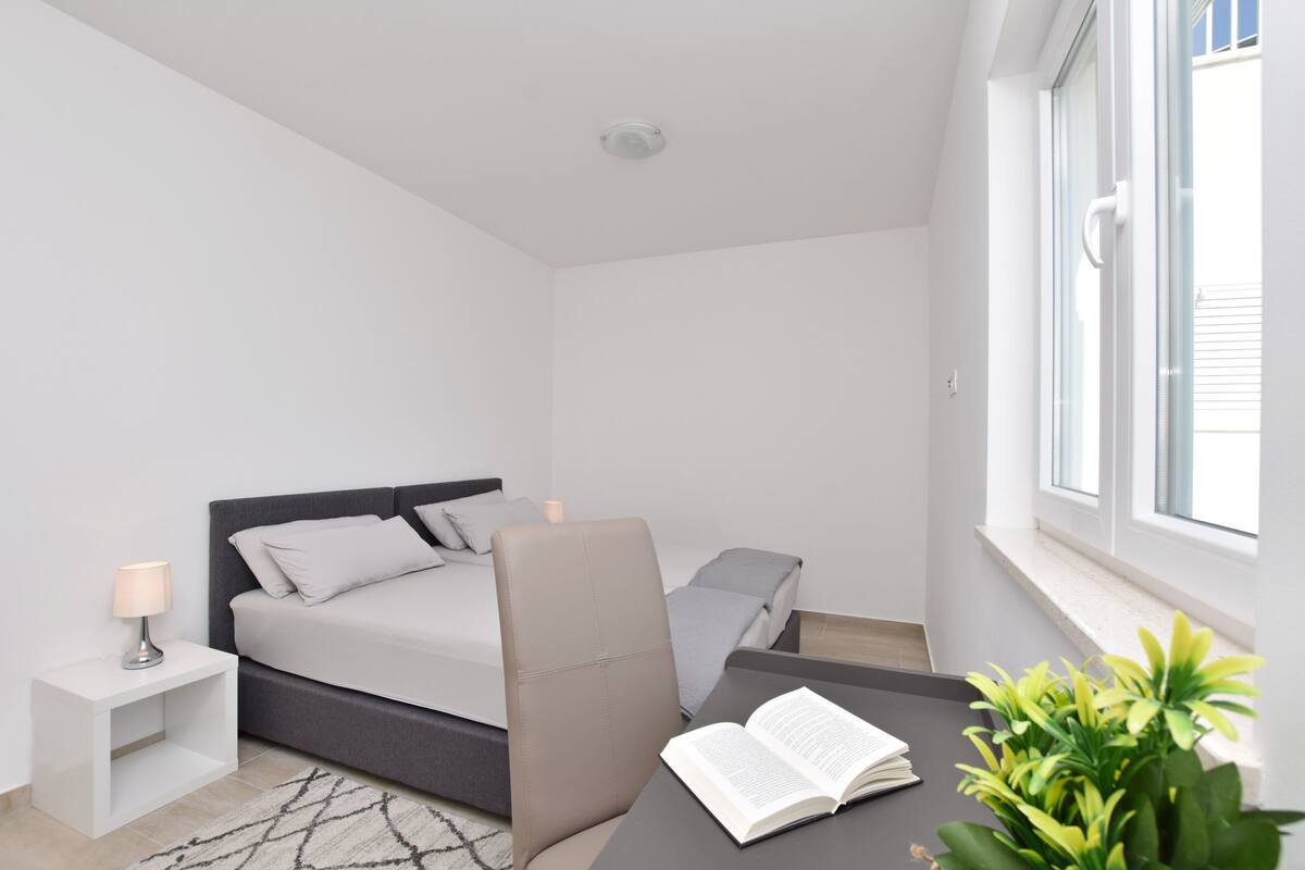 A modern bedroom with a bed, bedside table, chair, and a window.