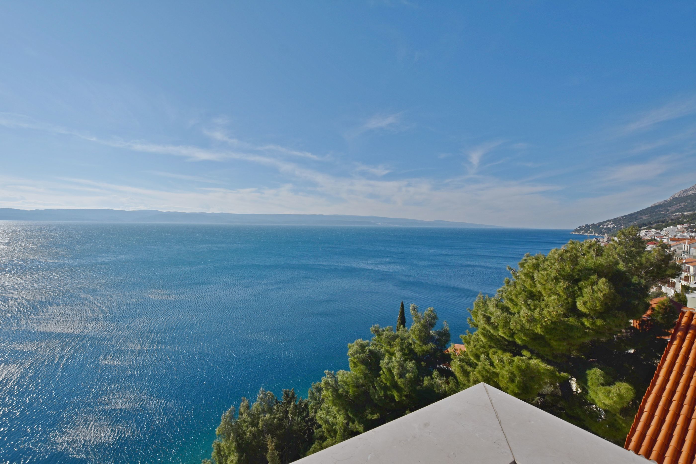 A coastal view with a clear sky, a body of water, and a building with a tiled roof.