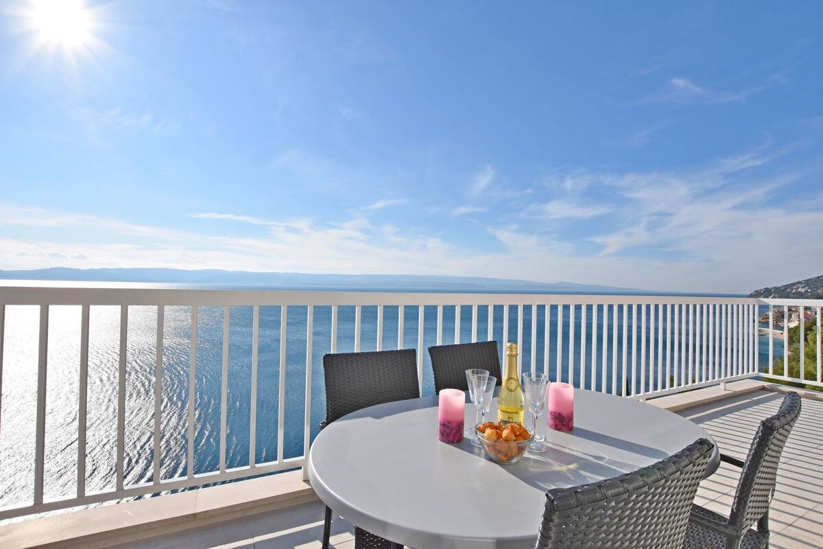 A round table with chairs on a balcony overlooking a body of water.