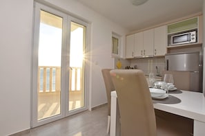 A modern kitchen with white cabinets, a stainless steel refrigerator, and a dining area with a table set for two. - Apartments Danolic (Omis)