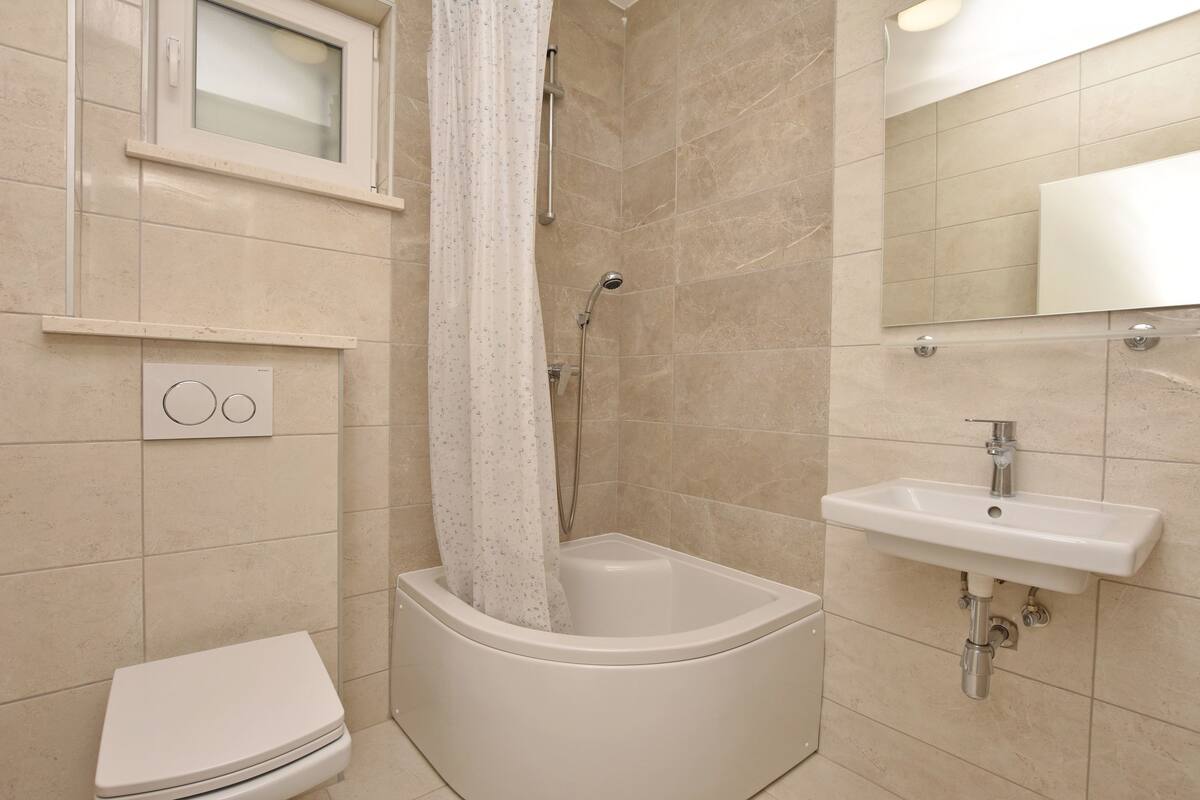 A bathroom with a bathtub, toilet, sink, and a window with a curtain.